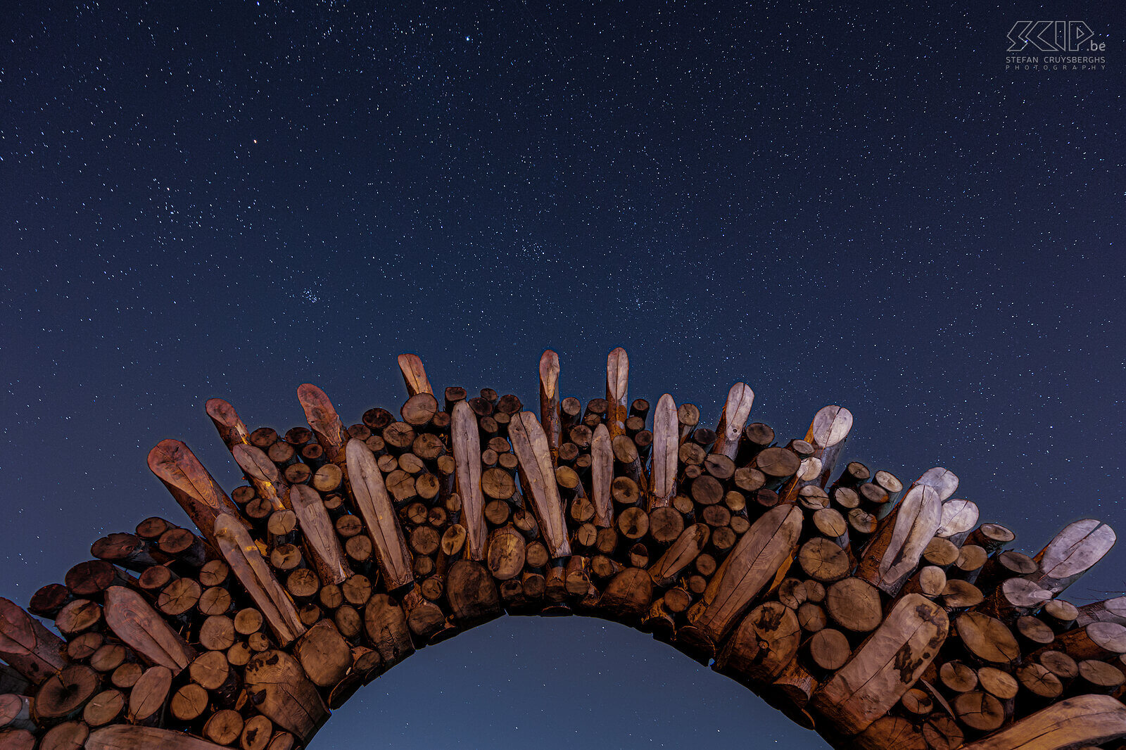 Hageland by night - Poort Chartreuzenbos in Holsbeek Een prachtige sterrenhemel aan de poort aan de rand van het Chartreuzenbos, gelegen in Holsbeek en Lubbeek. De houten poort is een mooi kunstwerk in de vorm van een zon.  Stefan Cruysberghs